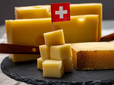 Swiss cheeses, block of medium-hard yellow cheese emmental or emmentaler with round holes and matured gruyere close up served in cubes as mountain top with Swiss flag.