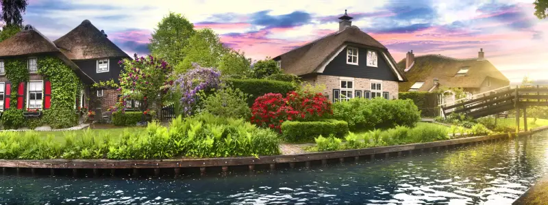 Landscape of Giethoorn village with water canals and rustic houses in netherland country wide banner or panorama. Old small brick house with thatched roof and wooden bridge. 